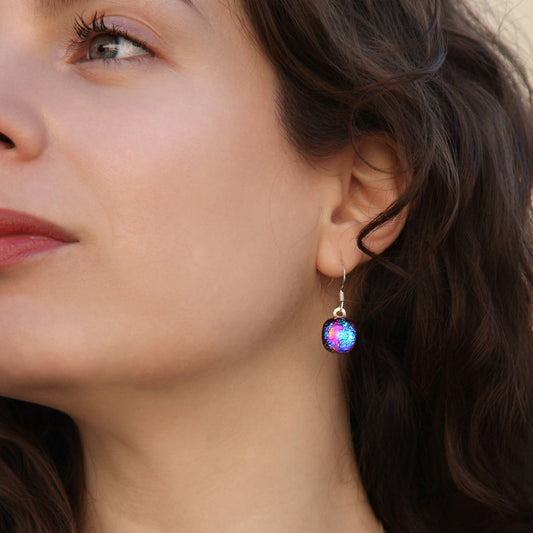 Close-up of model wearing round ripple-effect dichroic glass drop earrings in pink, blue and gold. Orb collection by Invoke London.