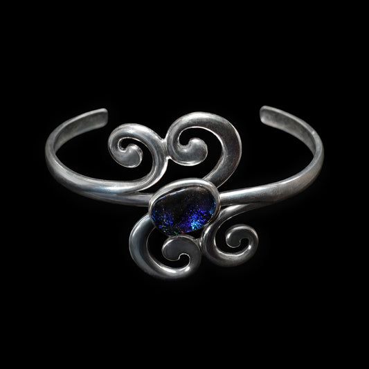 Silver scroll bracelet with a blue gemstone on a black background