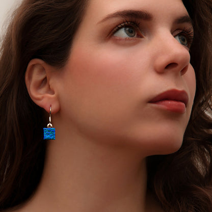Close-up of woman wearing square blue dew drop dichroic glass drop earrings from the Astra collection by Invoke London – handmade in London.