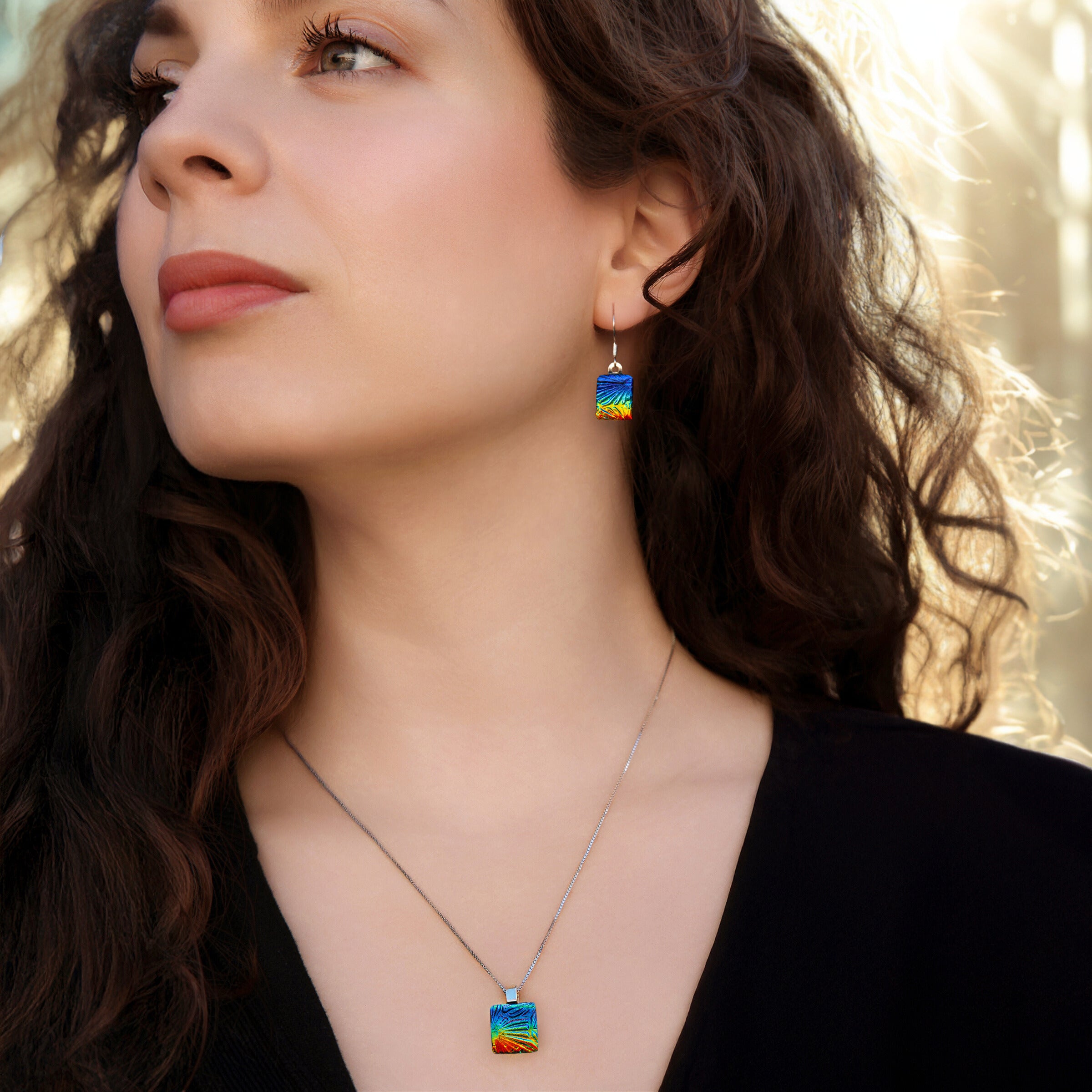Model wearing matching rainbow florentine dichroic glass drop earrings and pendant necklace in sunlight, handmade in London by Madiha Zaidi.
