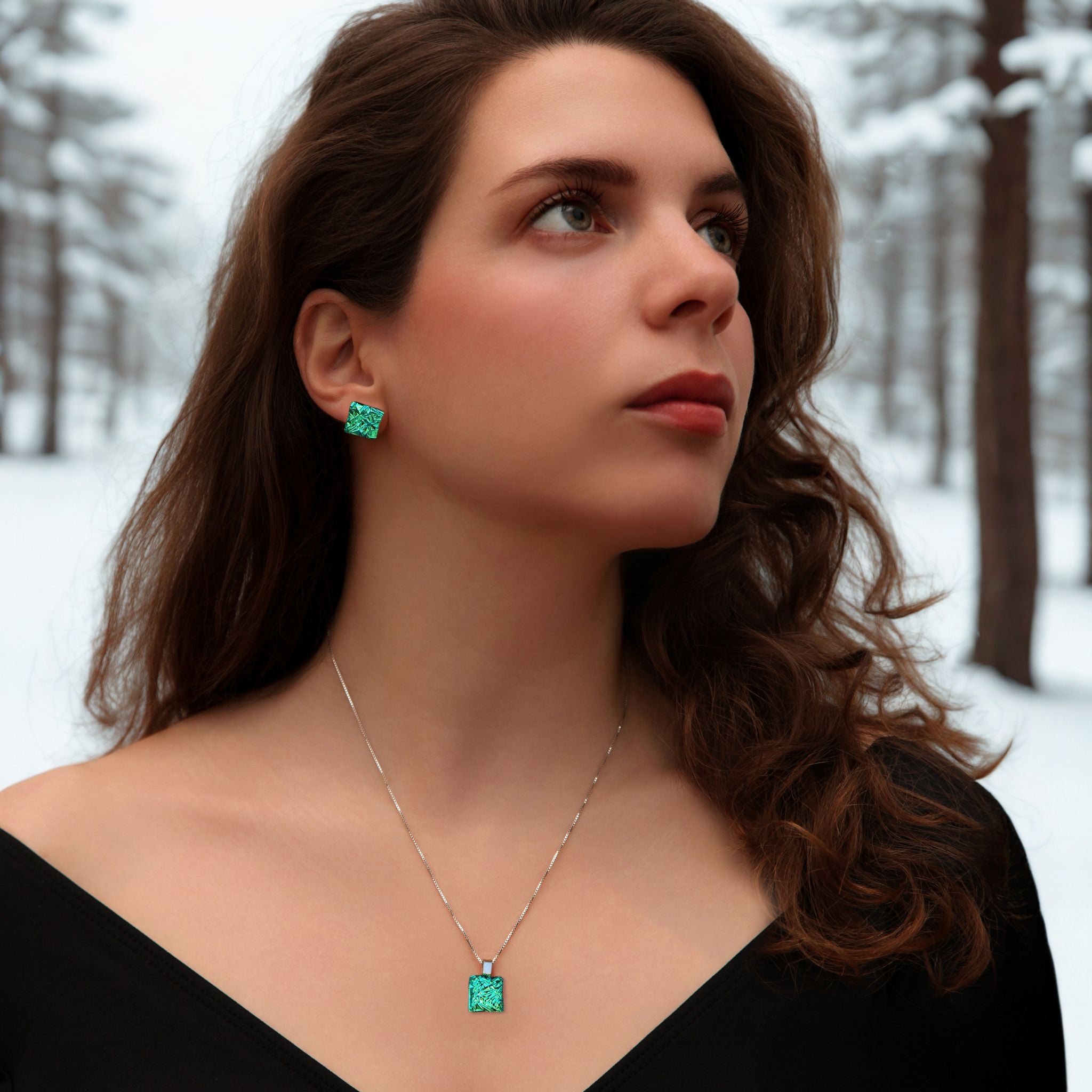 Woman wearing green earrings and a necklace in a snowy forest