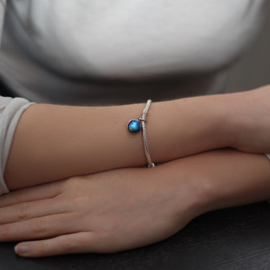 Close-up of a wrist wearing a silver bracelet with a blue gemstone.