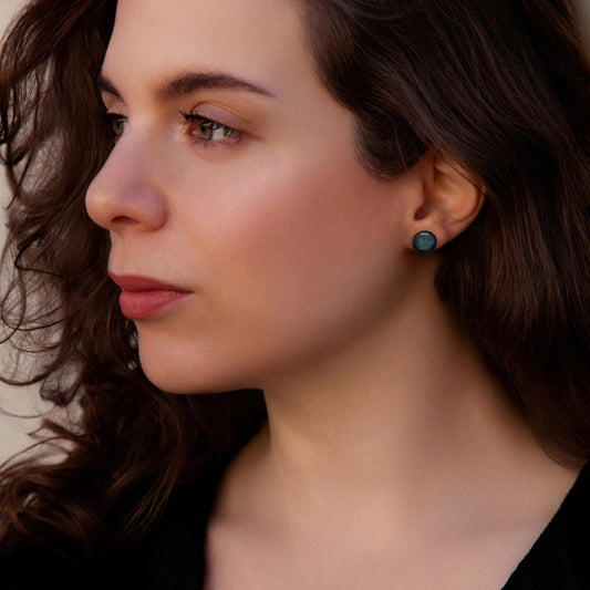 Close-up of a woman wearing green earrings with a neutral background