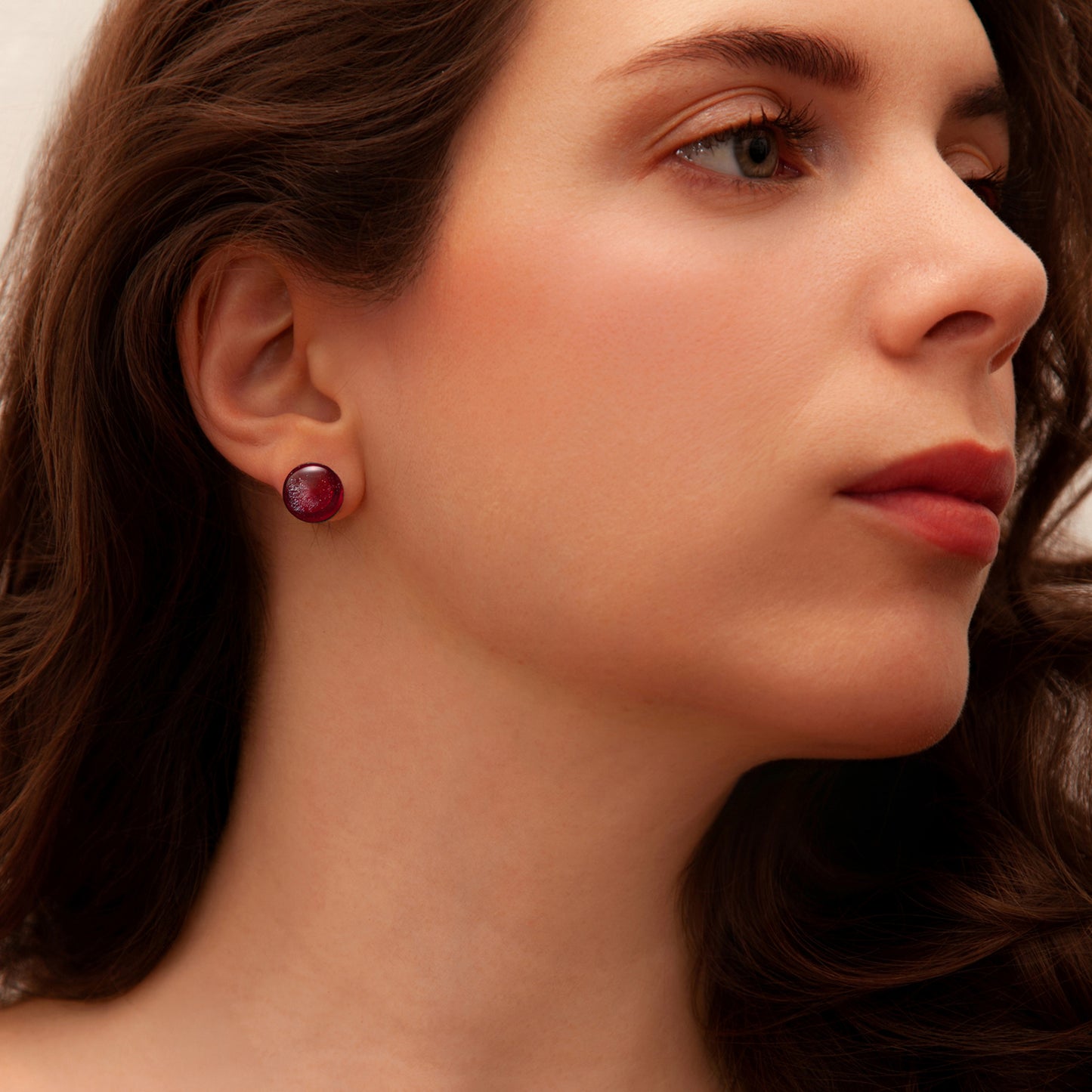 Close-up of a woman wearing a red earring with a neutral background