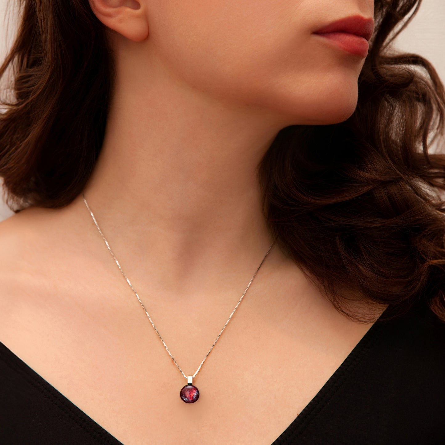 Close-up of a woman wearing a silver necklace with a red glass gemstone pendant.