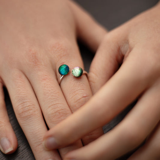 Close-up of a hand wearing a ring with two gemstones in pink and green.