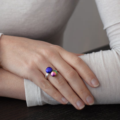Hand wearing a ring with two gemstones one in pink and the other in purple on a neutral background