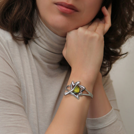 Woman wearing a silver bracelet with a green dichroic stone on a neutral background