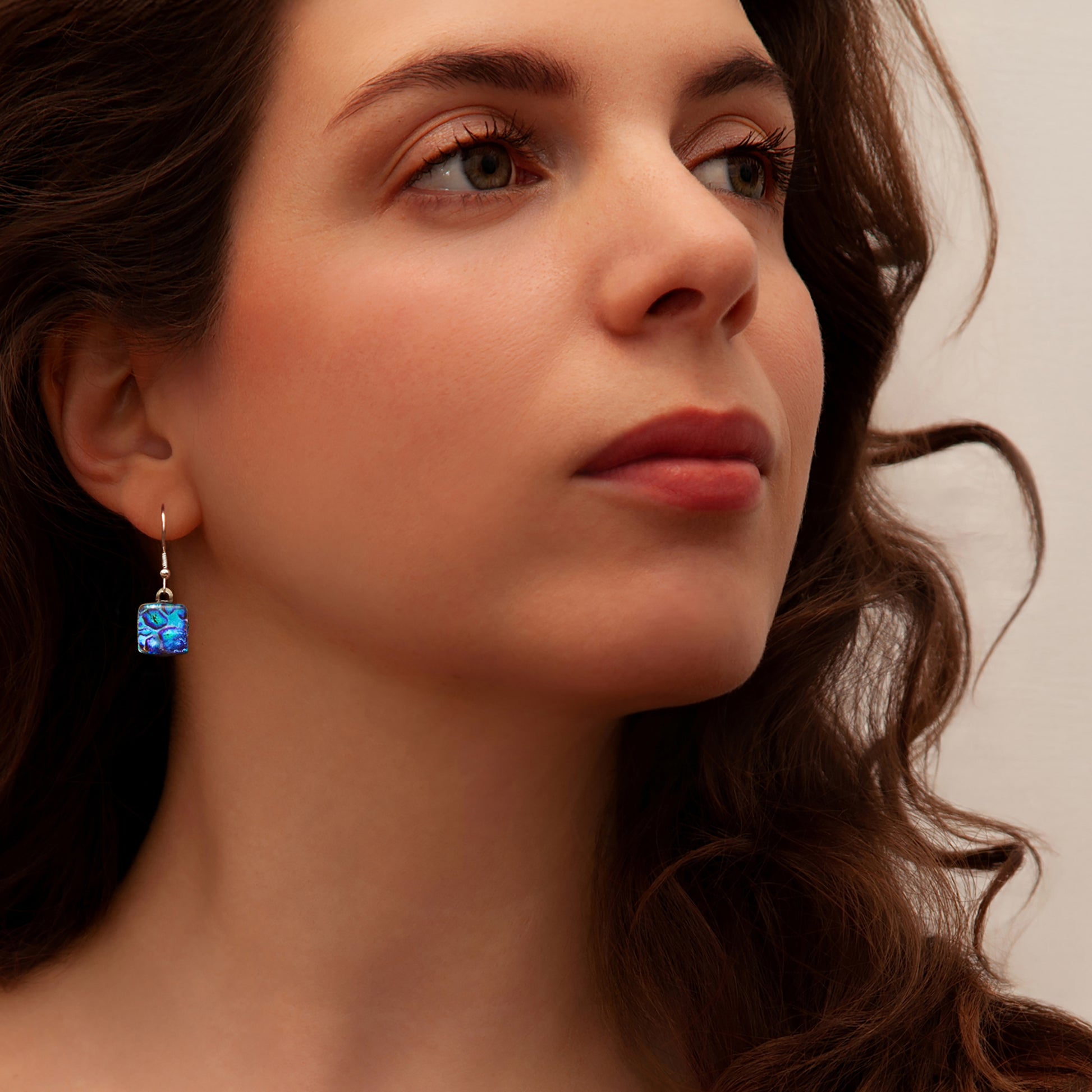 Close-up of a woman wearing blue cube drop earrings with a neutral background