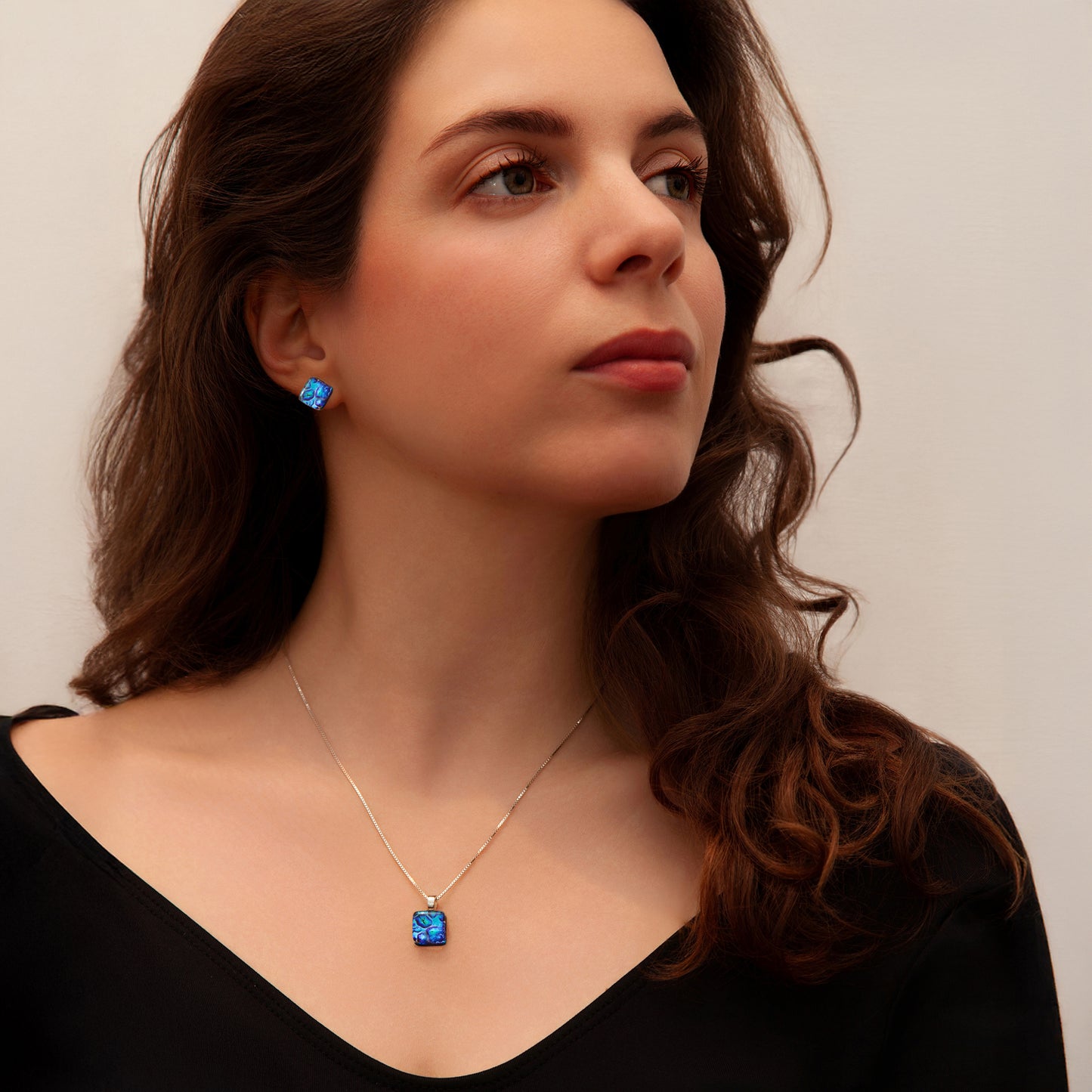 Woman wearing a blue cube necklace and matching earrings against a neutral background