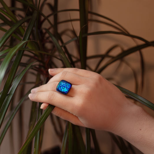 Hand wearing a blue ring holding a plant leaf with a blurred background