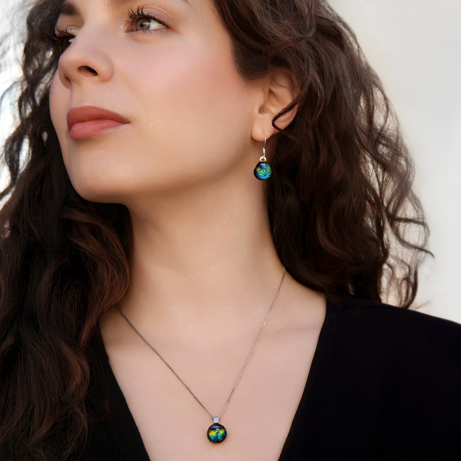 Model wearing matching green and gold ripple dichroic glass drop earrings and pendant necklace, handmade in London by Madiha Zaidi.