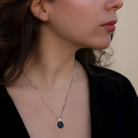 Close-up of a woman wearing a silver necklace with a black pendant with blue dots against a neutral background