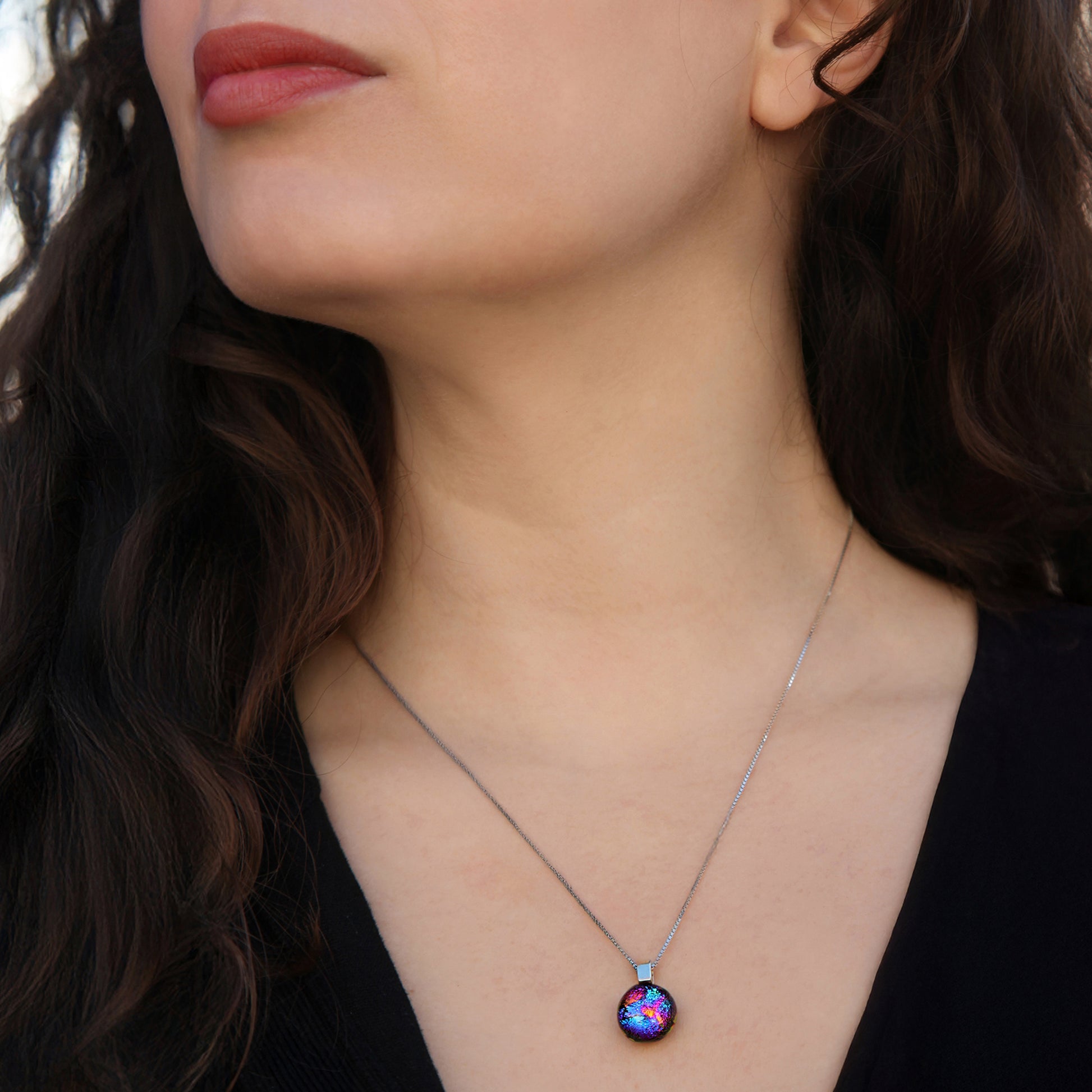 Close up of model wearing a necklace with ripple-effect dichroic glass in pink, blue, and gold, from the Orb Collection by Invoke London.
