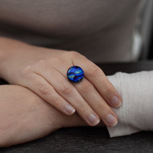 Hand wearing a blue and green ring on a dark surface