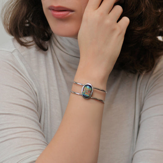 Person wearing a silver bracelet with a colorful stone on a neutral background