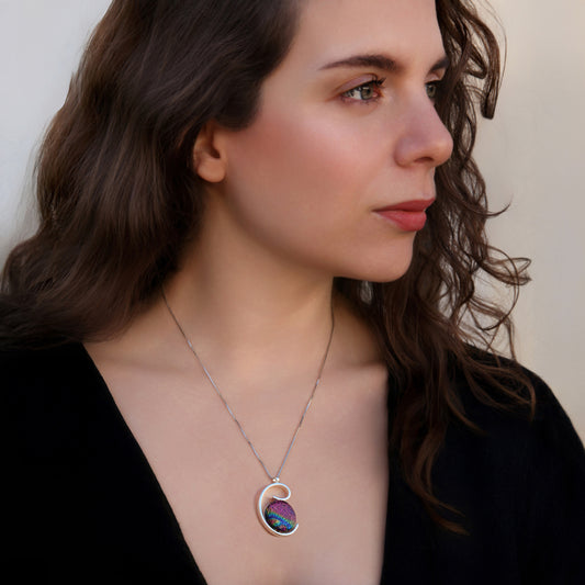 Woman wearing a silver spiral Stella necklace with a large round dichroic glass pendant in vibrant pink and blue tones by Invoke London.