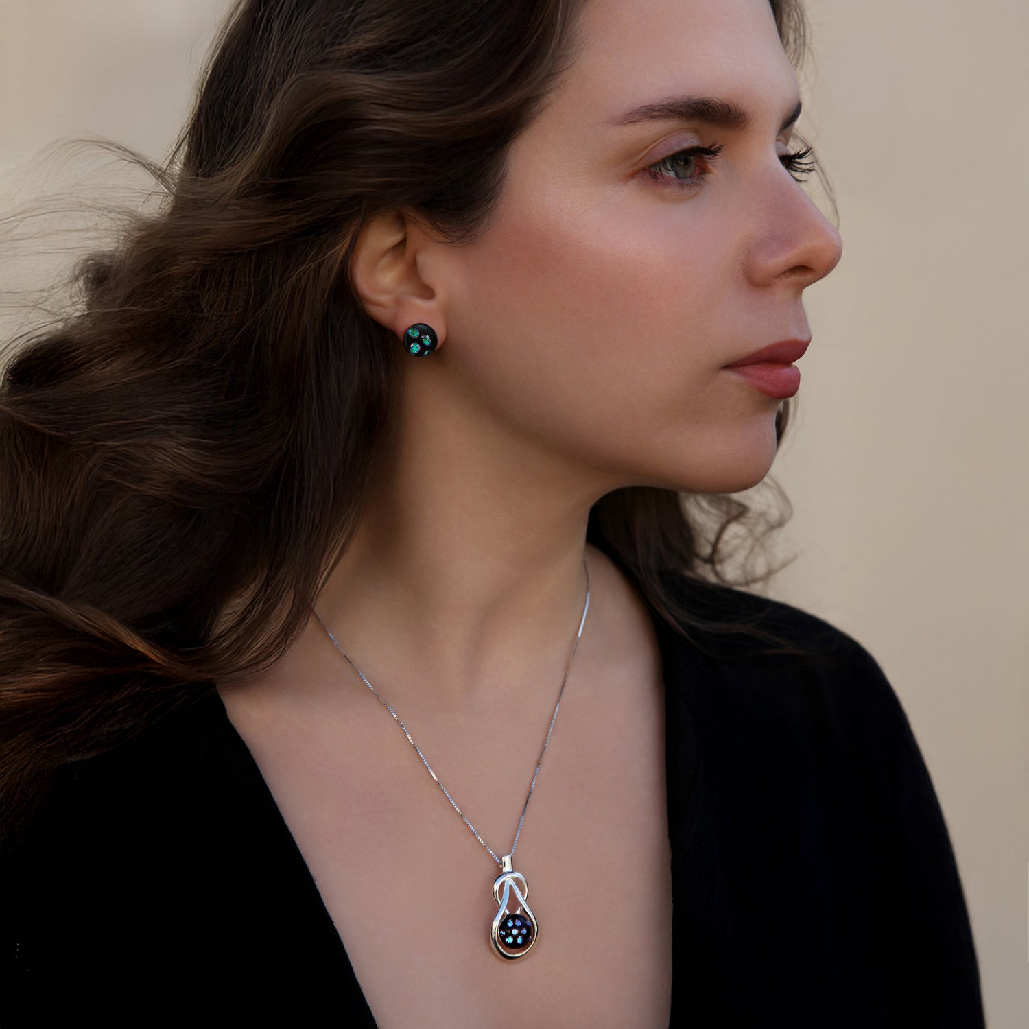 Model wearing a Stella Collection necklace by Invoke London, featuring a silver teardrop knot pendant necklace and matching Orb stud earrings with black fused glass and shimmering blue dichroic dots.
