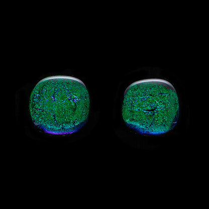 A pair of large, round, dark green dichroic glass stud earrings against a black background.