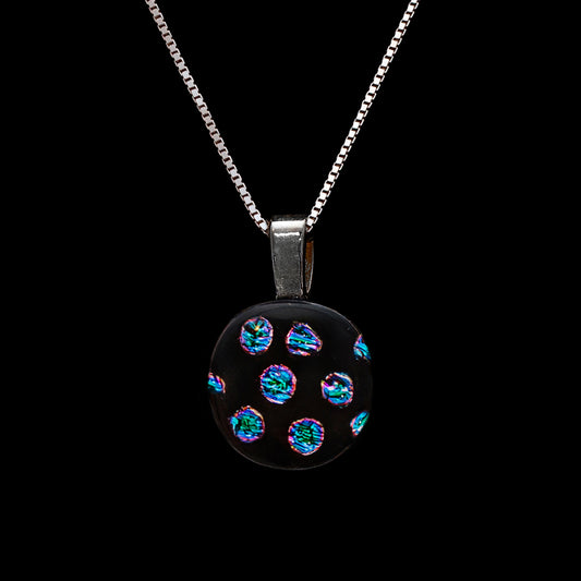 Round pendant necklace with a black fused glass base and shimmering blue and green dichroic dot pattern, handmade by Invoke London from the Orb Collection.