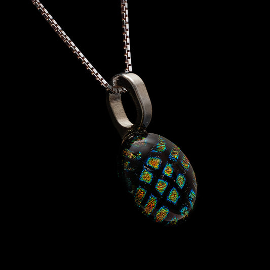Side view of round black dichroic glass pendant with red square shimmer on a sterling silver chain, handmade in London by Invoke London.